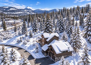 A two-story lodge with a snow-covered roof, surrounded by a dense forest of evergreen trees. - Serene home on 2 Acres, Minutes to Slopes, Private Hot Tub (Breckenridge)