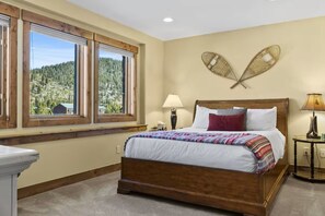 A bedroom with a large bed, a window with a view of a forest, and a wall-mounted decorative item. - Serene home on 2 Acres, Minutes to Slopes, Private Hot Tub (Breckenridge)