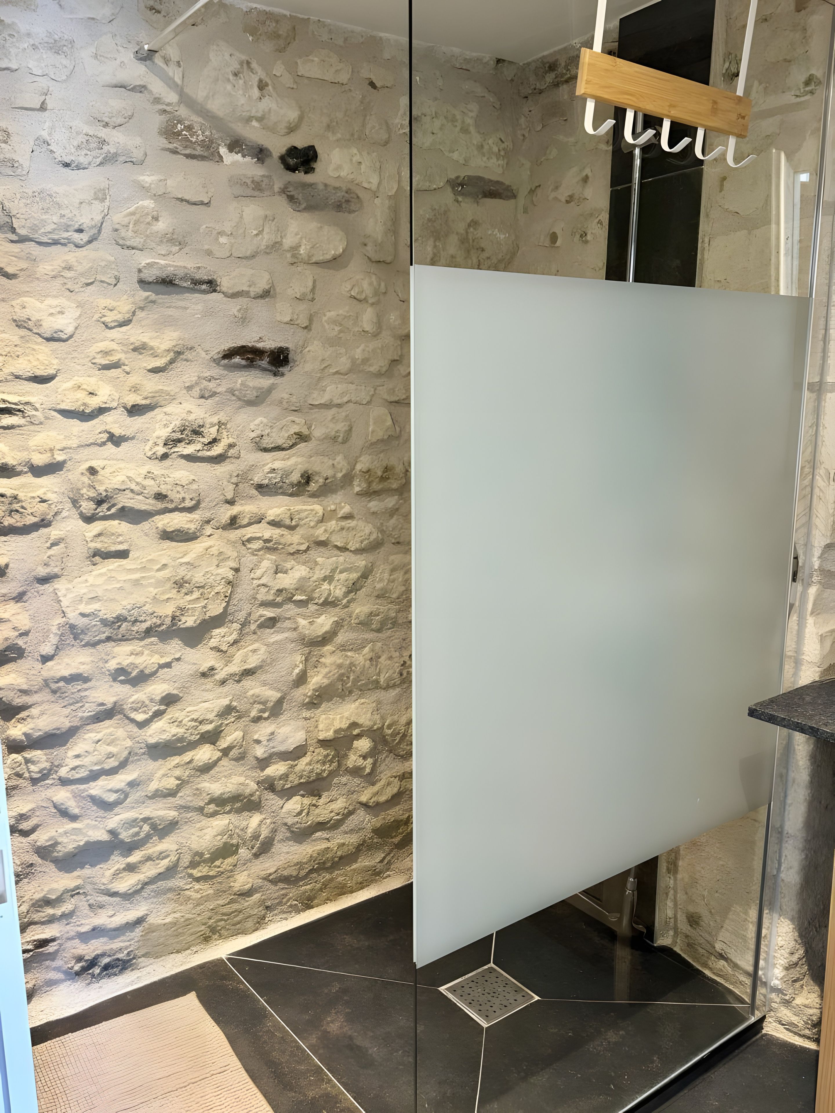 Un baño con pared de piedra, puerta blanca y suelo de baldosas negras.