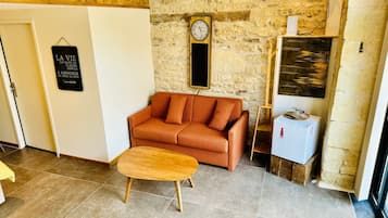 Une pièce chaleureuse avec un mur en pierre, un banc en bois, un canapé, une horloge et un petit réfrigérateur.
