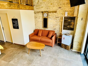 Habitación acogedora con pared de piedra, un banco de madera, un sofá, un reloj y un refrigerador pequeño.