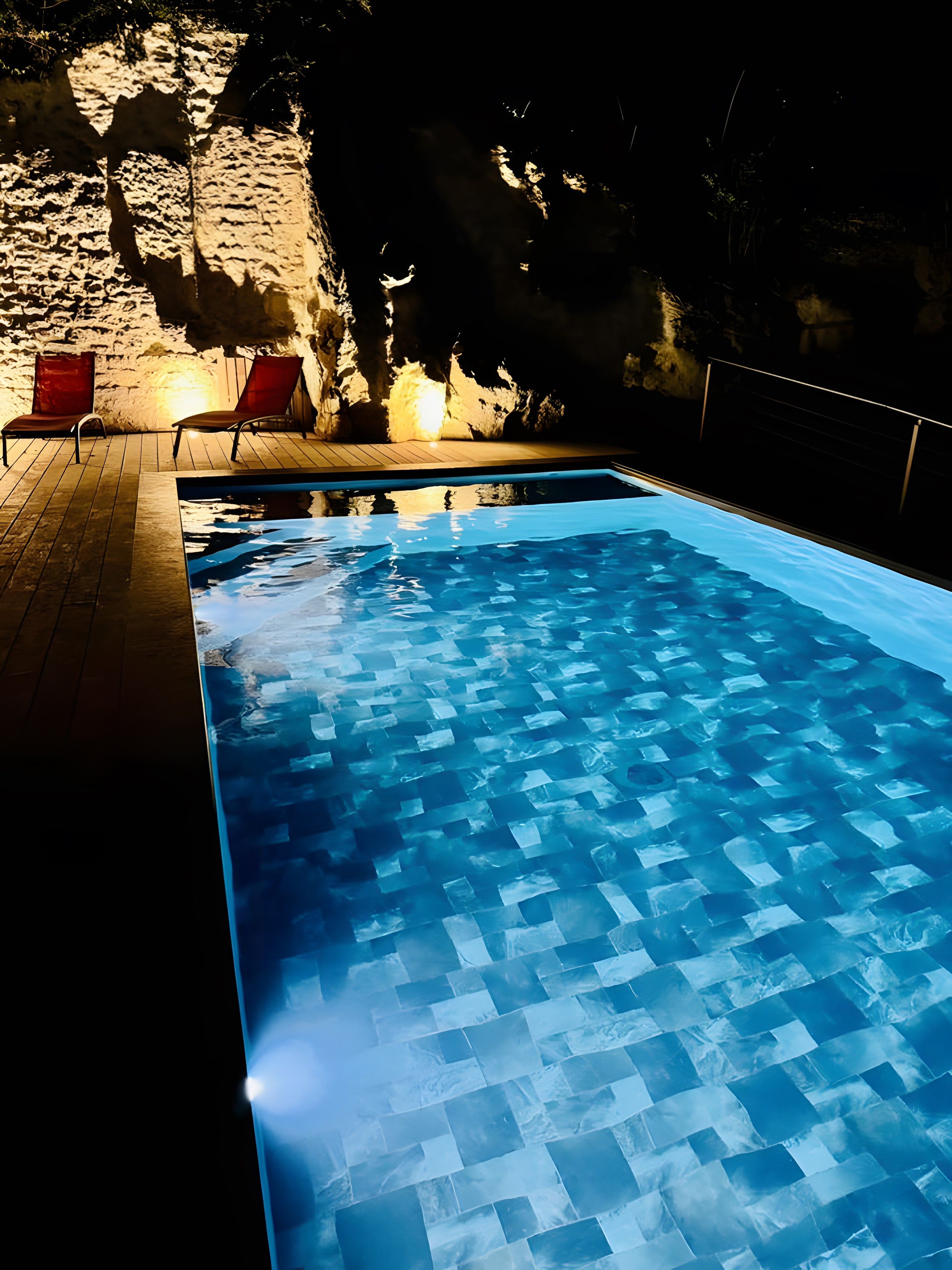 Ein Schwimmbecken mit Fliesenboden, umgeben von einer Holzterrasse und roten Stühlen.