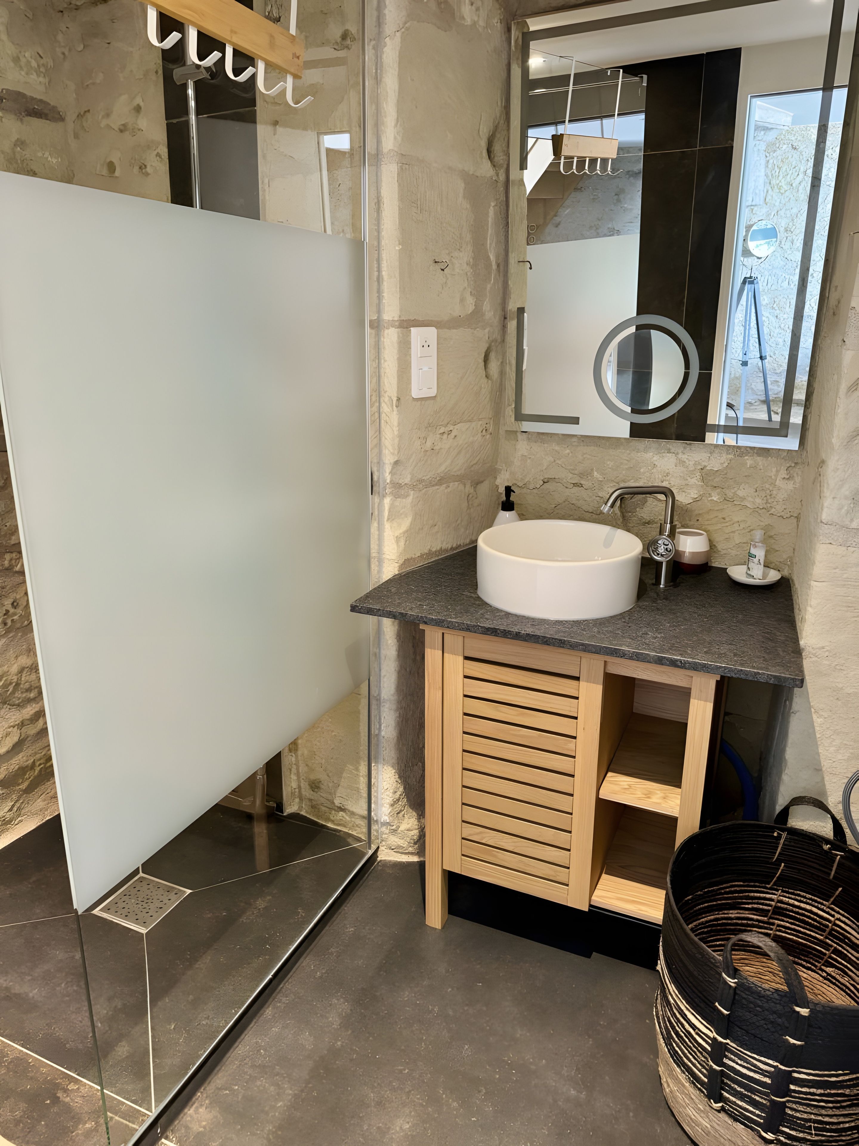 Ein Badezimmer mit weißem Waschbecken, Holzschrank und Spiegel mit rundem Rahmen.