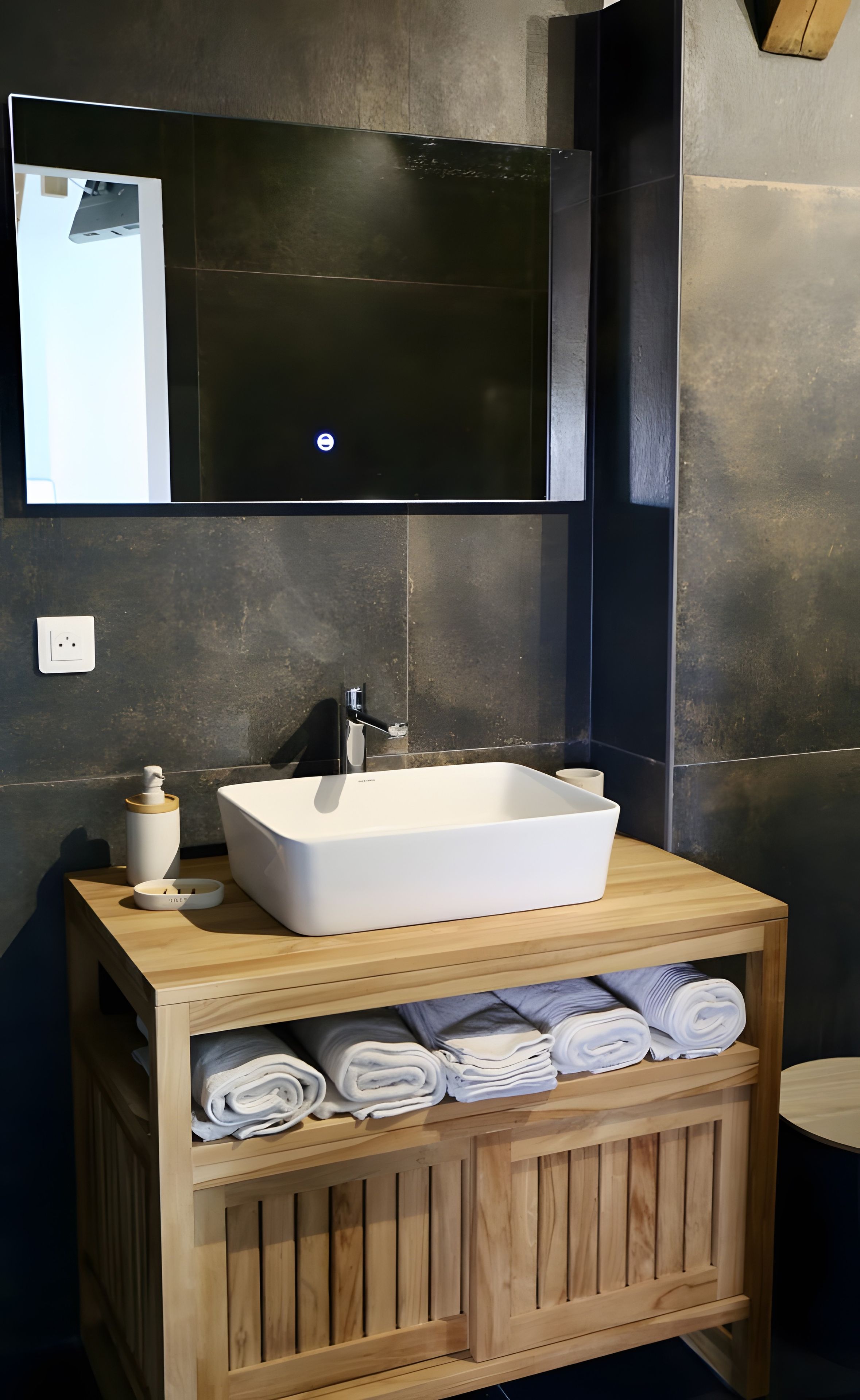 A modern bathroom with a large mirror, a white sink, and a wooden vanity with towels.
