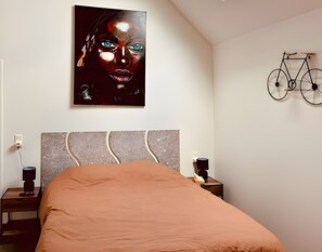 Een slaapkamer met een bed, een hoofdbord, een aan de muur bevestigde fiets, nachtkastjes en een kunstwerk aan de wand.