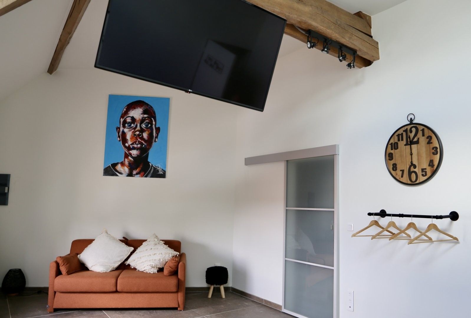 Ein Wohnzimmer mit einer Couch, einem Fernseher, einer Uhr und einem an der Wand befestigten Kleiderhaken.