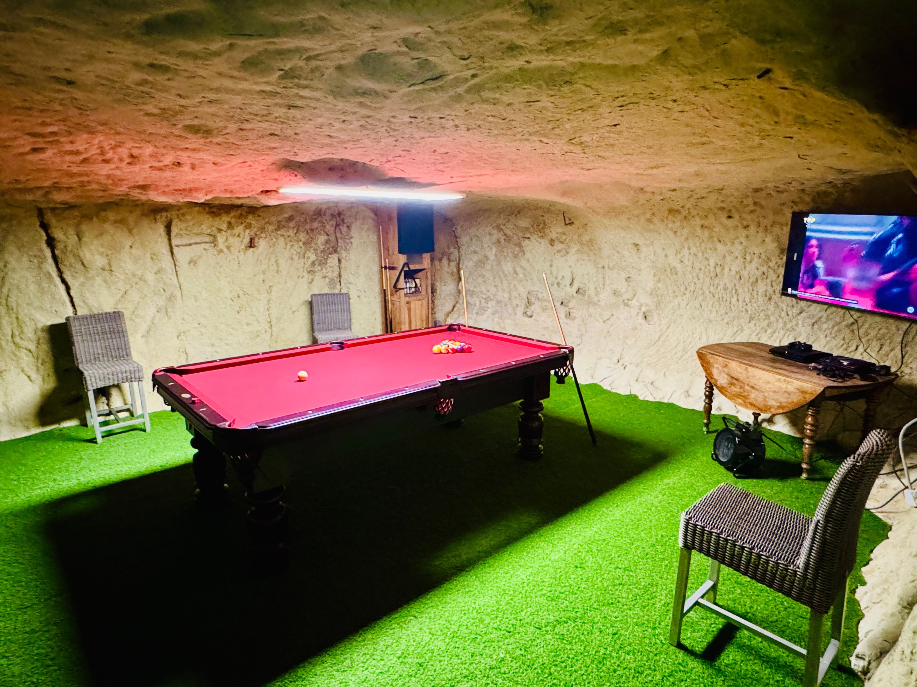 Une table de billard recouverte d’un drap vert, une chaise et un téléviseur fixé au mur.