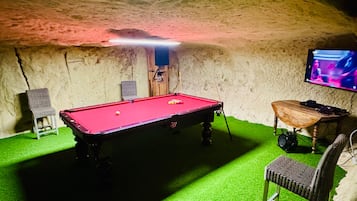 Une table de billard recouverte d’un drap vert, une chaise et un téléviseur fixé au mur.