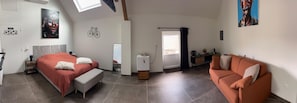 Un dormitorio moderno con cama, banca, cómoda y una mesita con ventilador.