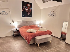 Un dormitorio con cama, lámparas de noche, mesita de noche, un banco, una bicicleta colgada en la pared y un cuadro grande.