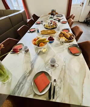 Een gedekte eettafel met borden, bestek en diverse soorten eten, waaronder fruit en gebak.