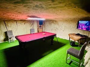 Taula de bitlles amb feliç verd, una cadira i un televisor fixat a la paret.