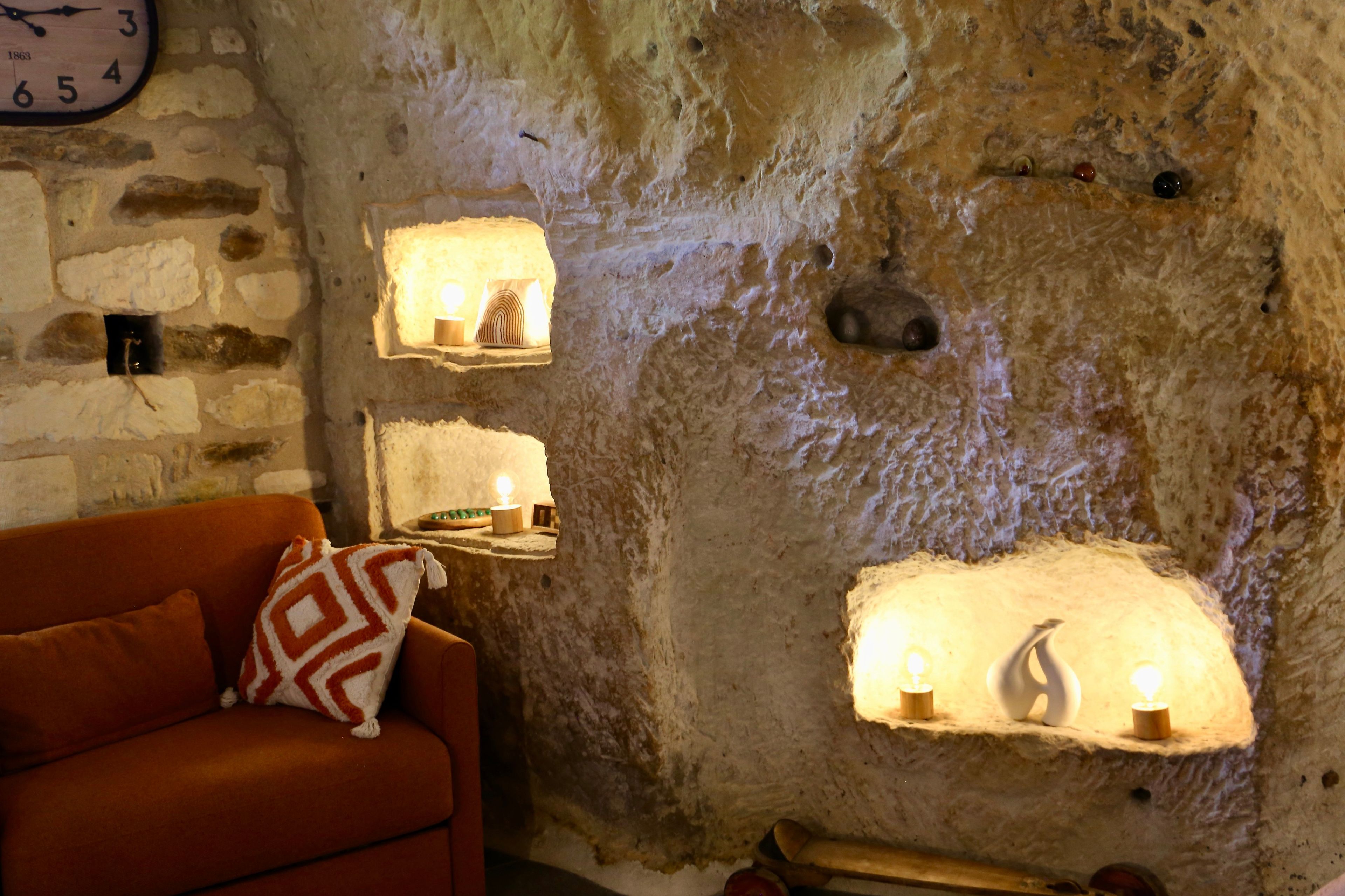 A cozy room with a stone wall, a clock, and a sofa with a patterned cushion.