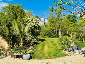 Un jardí amb un camí de grava, diferents plantes, una panxa i estàtues decoratives.
