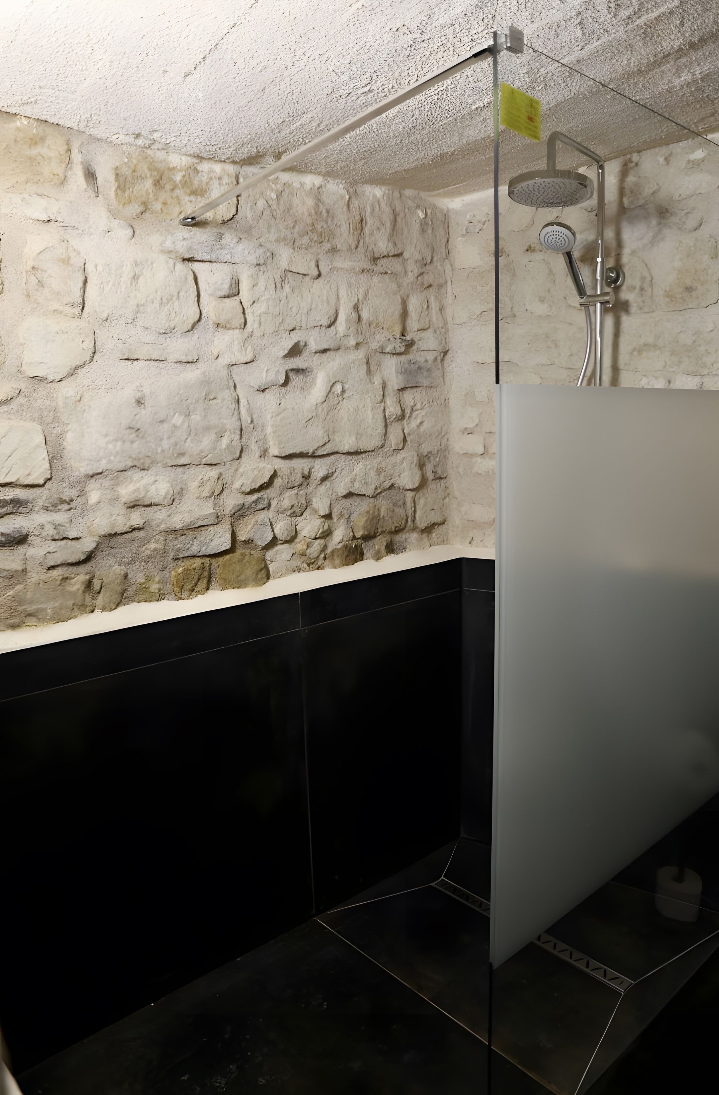 Un baño con pared de piedra, piso de baldosas negras y zona de ducha.
