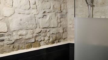 Un baño con pared de piedra, piso de baldosas negras y zona de ducha.