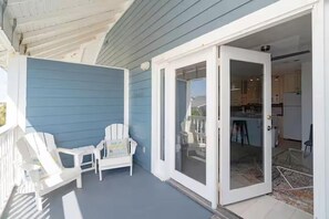 A covered porch with two white Adirondack chairs, a sliding glass door leading to a kitchen area. - ☀️Summer Breeze 302 | Gulf Views~Pool+Hot Tub~Balcony~Walk to Beach⛱️ (Miramar Beach)