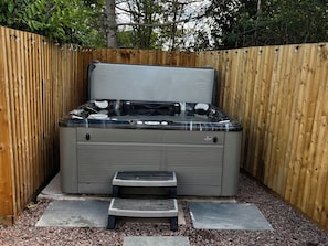 A hot tub with a wooden fence enclosure, a step leading up to it, and gravel flooring. - Meadow View Cottage (Gloucester)