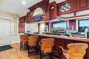 Un espace bar agrémenté d’une enseigne indiquant « Grande Vista », de tabourets de bar en bois et d’un comptoir où sont exposées diverses bouteilles et verres.