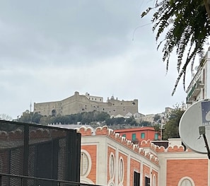 A historic building with a fortified structure on a hill, surrounded by modern buildings with decorative architecture. - Vrbo Property (Napoli)