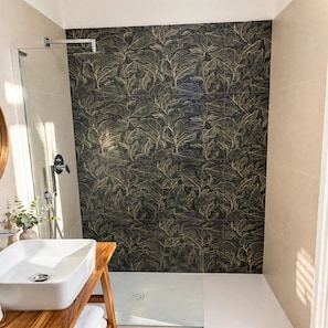 A bathroom with a white sink, a wooden vanity, a glass shower enclosure, and a dark patterned wall. - Vrbo Property (Napoli)