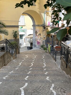 A narrow cobblestone street with an archway leading to a building with a pharmacy sign. - Vrbo Property (Napoli)
