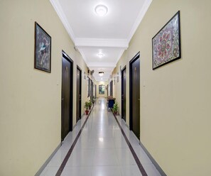 A hotel hallway with doors, potted plants, and artwork on the walls. - Deluxe Hotel Radhika Inn (Danapur)