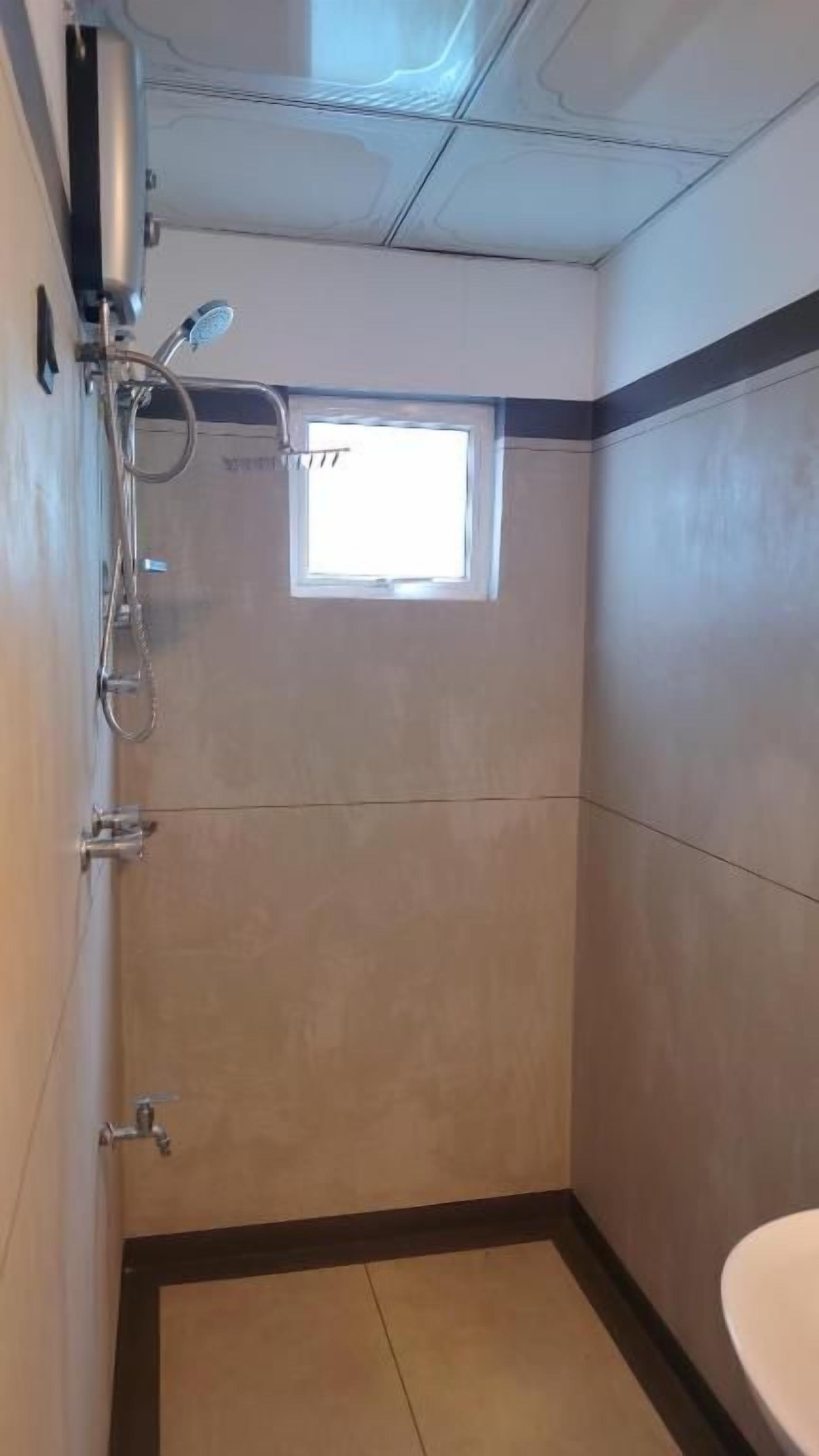 Un baño pequeño con ducha, ventana y lavamanos.