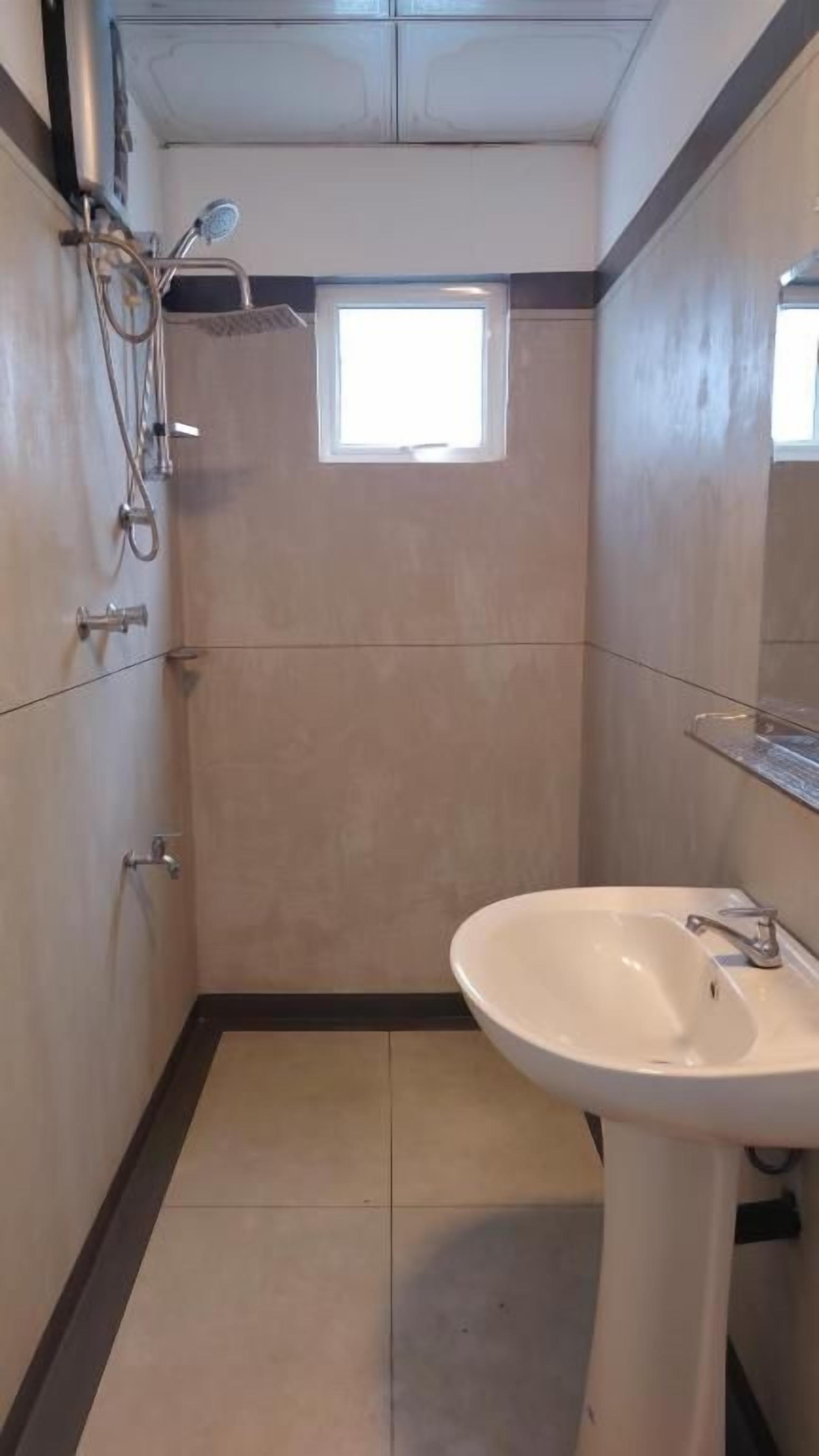 A bathroom with a shower, a sink, and a small window.