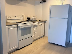 Eine Küche mit weißem Herd, Backofen und Kühlschrank, Holzschränken und einem hellen Boden.