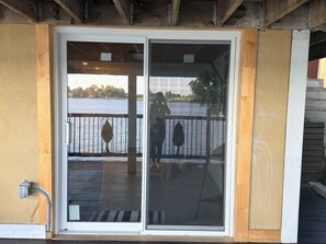 A sliding glass door leading to a deck with a view of a body of water and a dock. - Cozy Current Chalet with the backyard facing  Ottawa River (Montebello)
