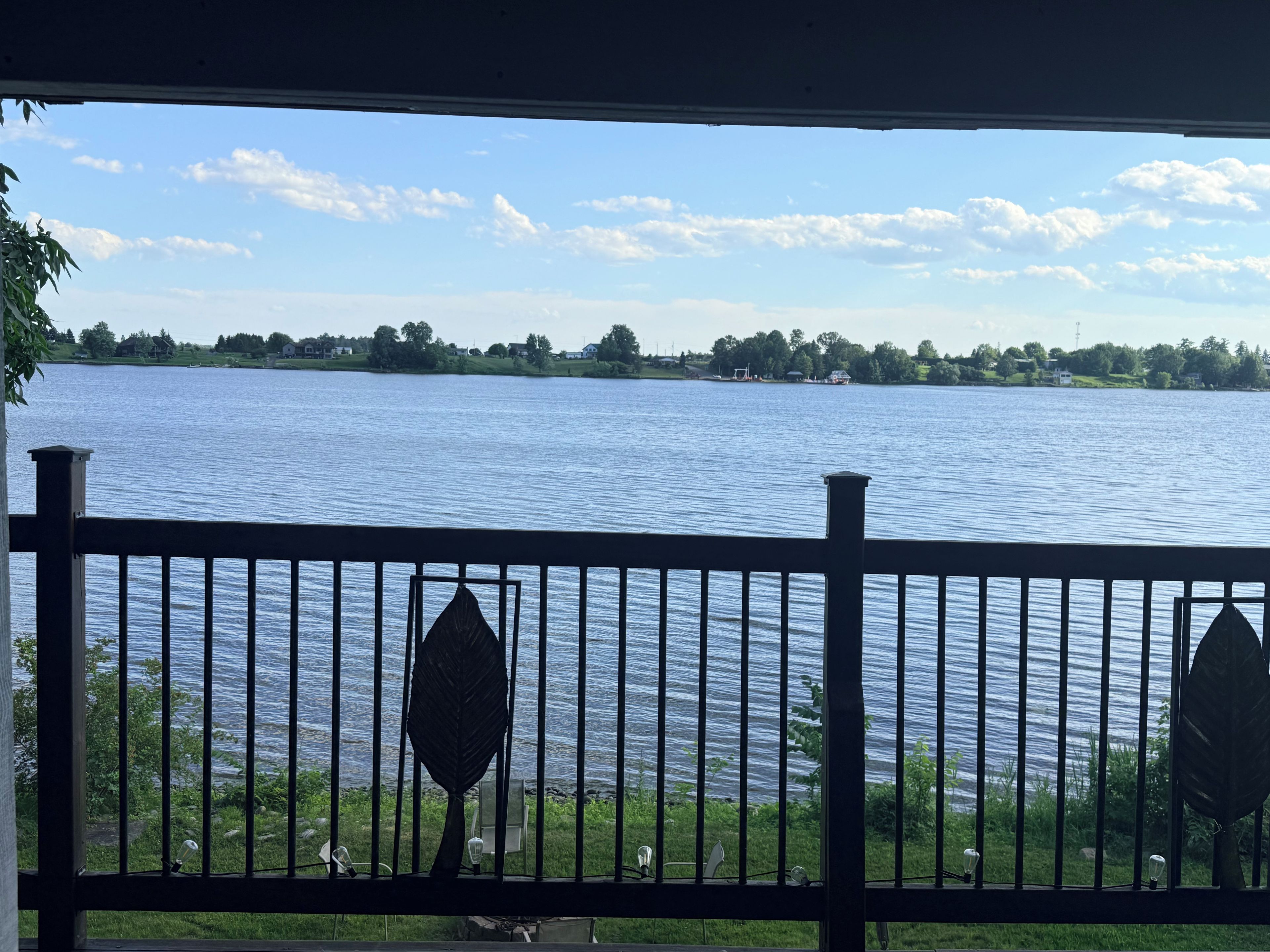 Uitzicht op een meer vanaf een balkon met een balustrade, een heldere lucht en verafgelegen bomen.