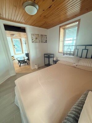 Un dormitorio con una cama grande, una mesita, una silla y un ventanal.