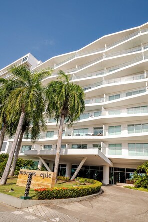 A multi-story building with a modern architectural design, featuring a prominent entrance with palm trees and a sign. - Comfortable Apartment Near the sea in Cartagena (Cartagena)