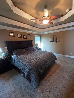 Quarto com uma cama grande, ventilador de teto, mesa de cabeceira e luminária na parede.