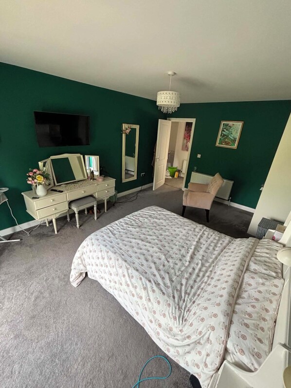 A bedroom with a bed, dresser, mirror, and a television on the wall.