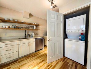 A compact kitchen with a dishwasher, a washing machine, and a wooden countertop. - Park Place, Carriage B - Ground‑Floor Courtyard Retreat Near Forsyth Park (Savannah)