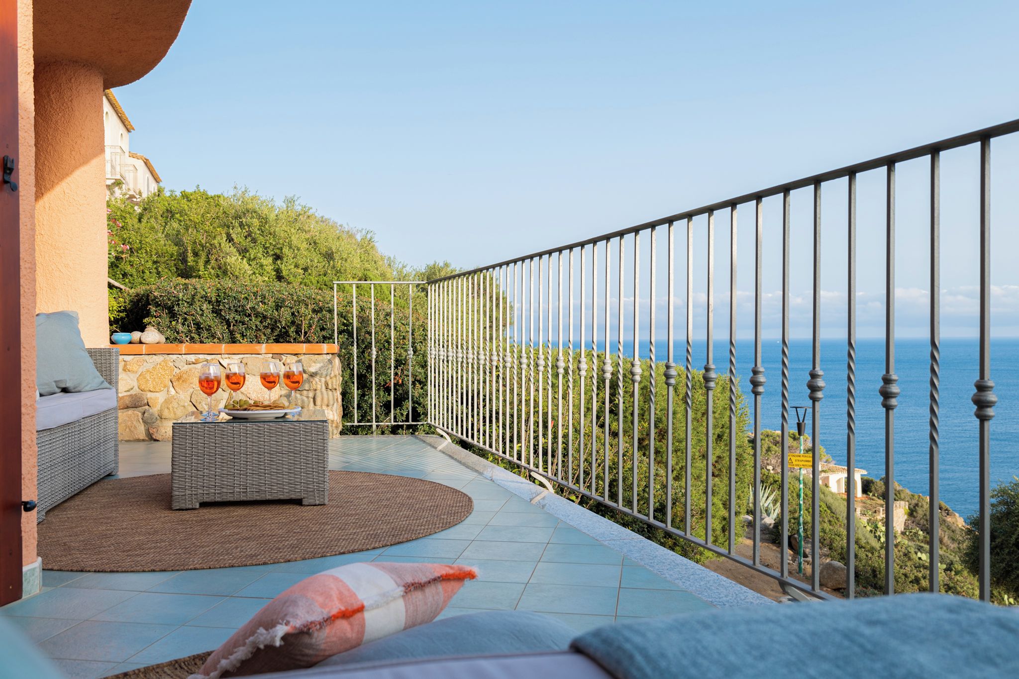 A balcony with a wicker sofa, a round rug, and a stone wall.