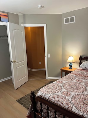 A bedroom with a bed, a nightstand with a lamp, a door leading to another room, and a wall-mounted vent. - A pleasant 3-bedroom house in a peaceful, quiet neighborhood in Milford (Milford)