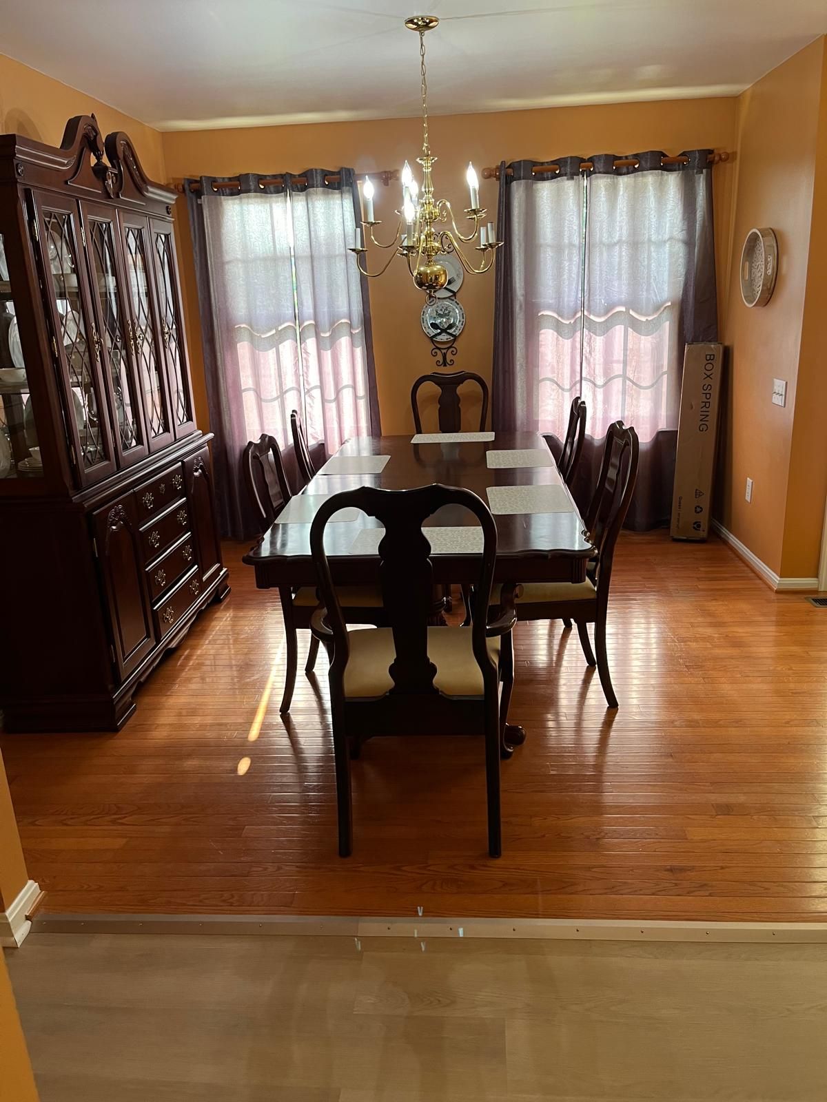 Une salle à manger avec une table en bois, des chaises, un lustre, des rideaux et un buffet.