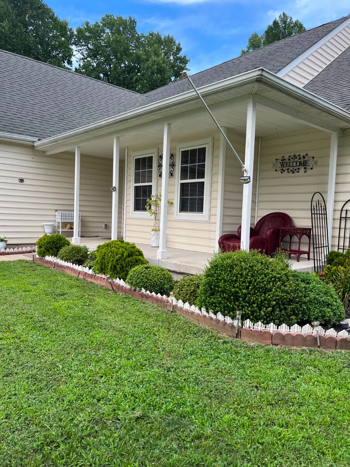 A two-story house with a covered porch, a welcome sign, and a well-maintained lawn.