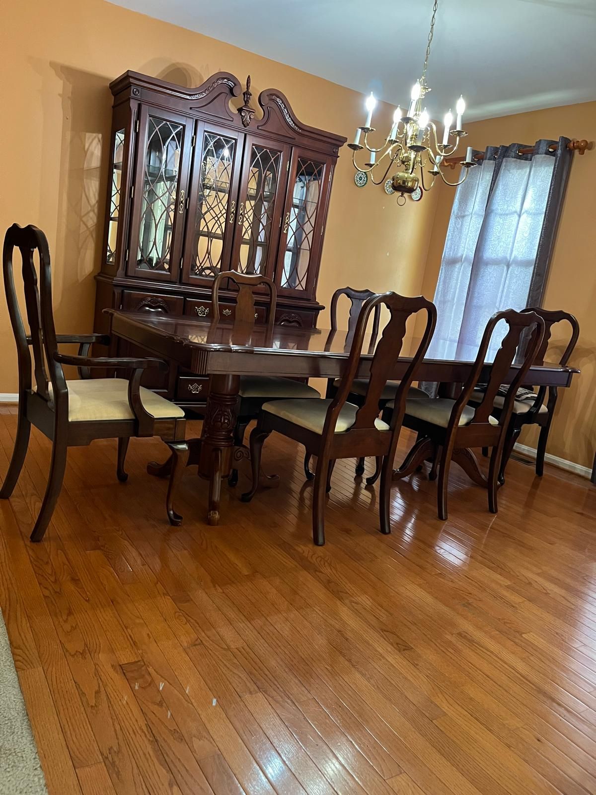 Comedor con una mesa y sillas de madera, un aparador con cubierta de vidrio y una araña.