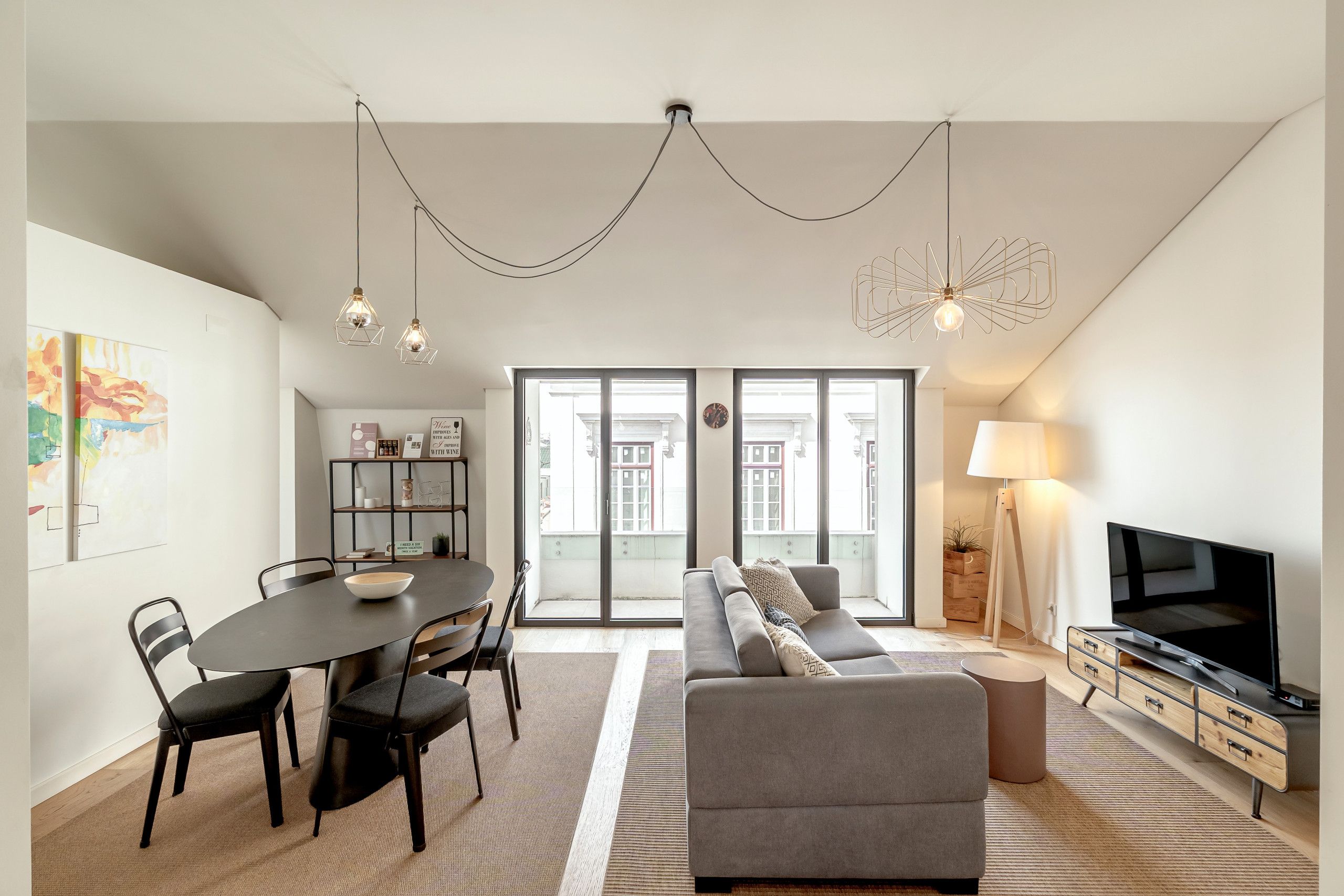 A modern living room with a sofa, dining table, chairs, a TV, and a bookshelf.