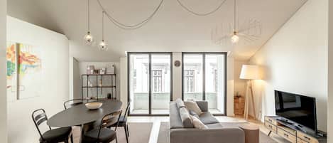 A modern living room with a sofa, dining table, chairs, a TV, and a bookshelf.