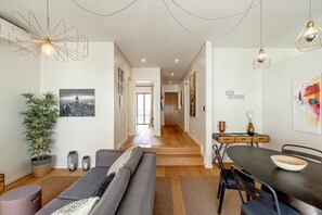 Un salon moderne avec un canapé, une table à manger et des chaises, un escalier menant à une autre pièce et un tableau représentant un paysage urbain accroché au mur.