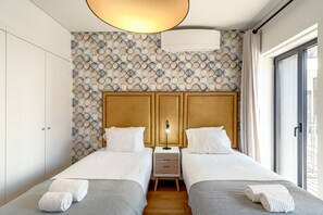 A hotel room with two beds, a nightstand, a lamp, and a view of the outside. - Bairro Alto Modern W/ Terrace by Homing (Lisbon)
