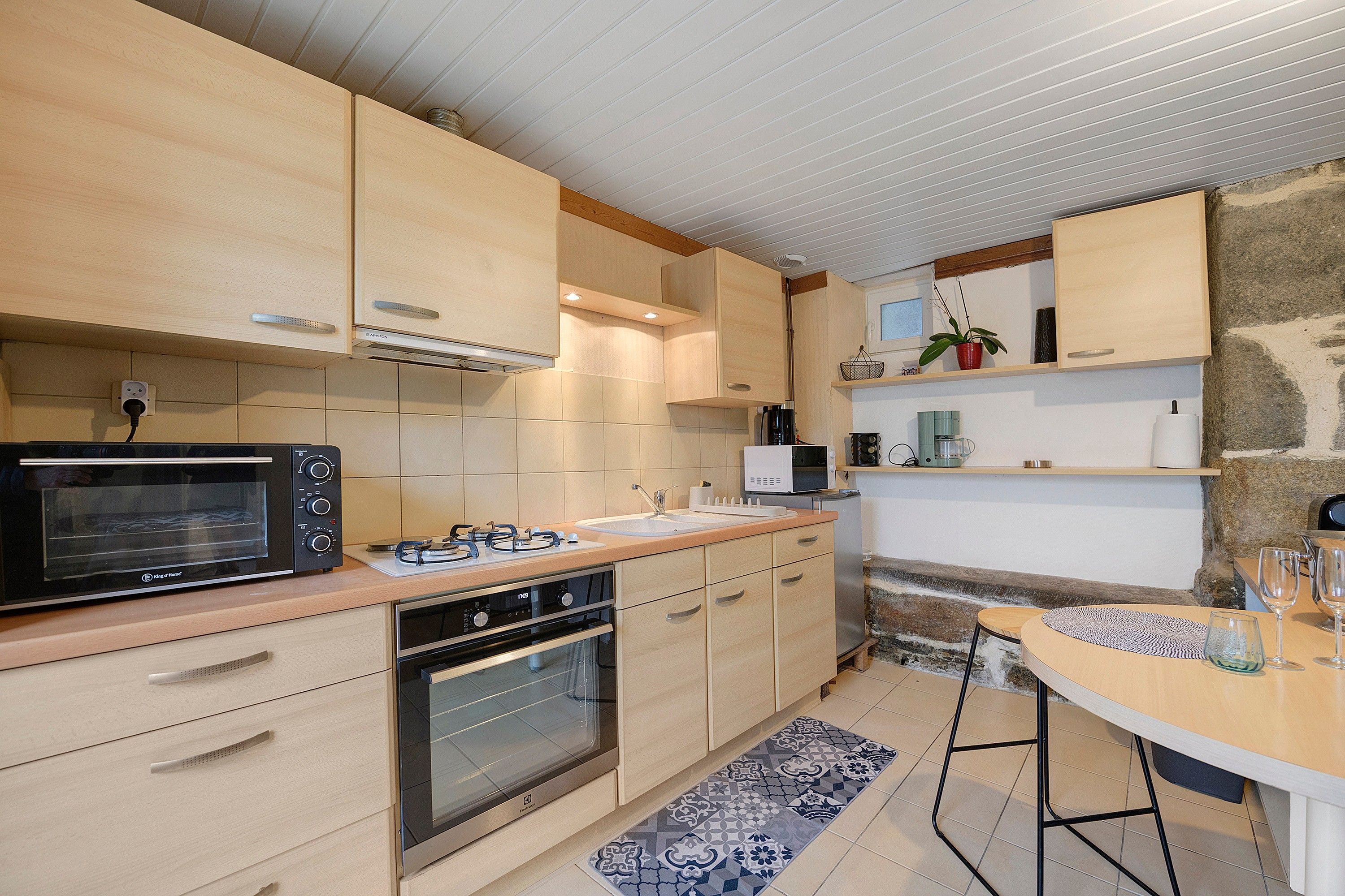 Une cuisine moderne avec des meubles en bois, un four encastré, un four à micro-ondes et un coin repas comprenant une table et des chaises.