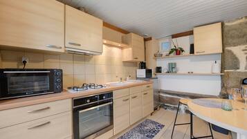 Une cuisine moderne avec des meubles en bois, un four encastré, un four à micro-ondes et un coin repas comprenant une table et des chaises.
