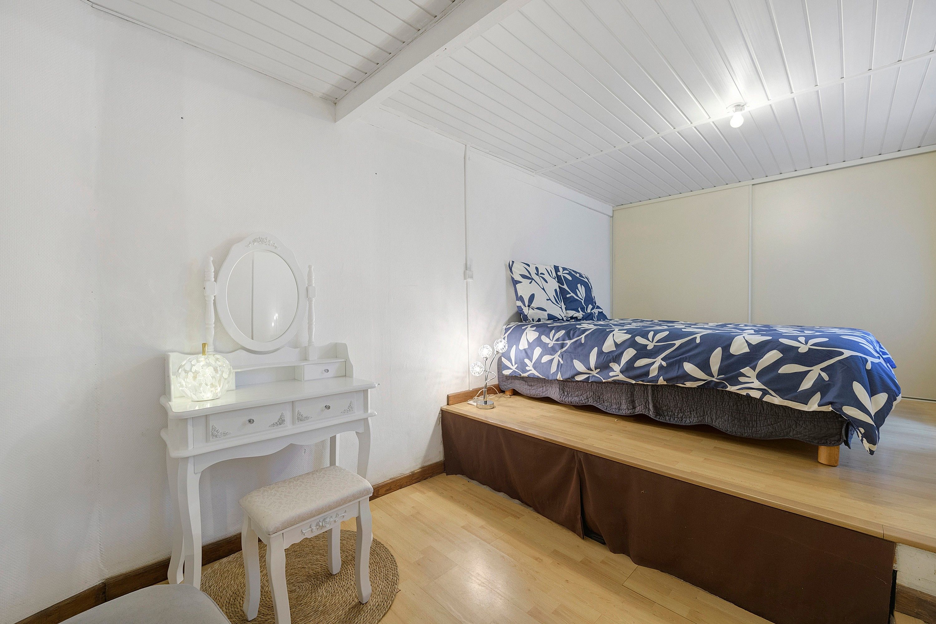 Een slaapkamer met een bed, een kaptafel met spiegel en een klein krukje.