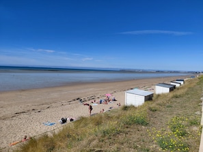 Una playa con gente tomando el sol y nadando, una hilera de cabañas de playa y un cielo despejado.